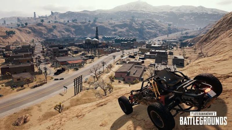 "A scenic view of Miramar, PUBG Mobile's desert map, highlighting a buggy parked on a sandy hill overlooking a sprawling urban area with industrial structures, power lines, and rugged mountainous terrain in the background."