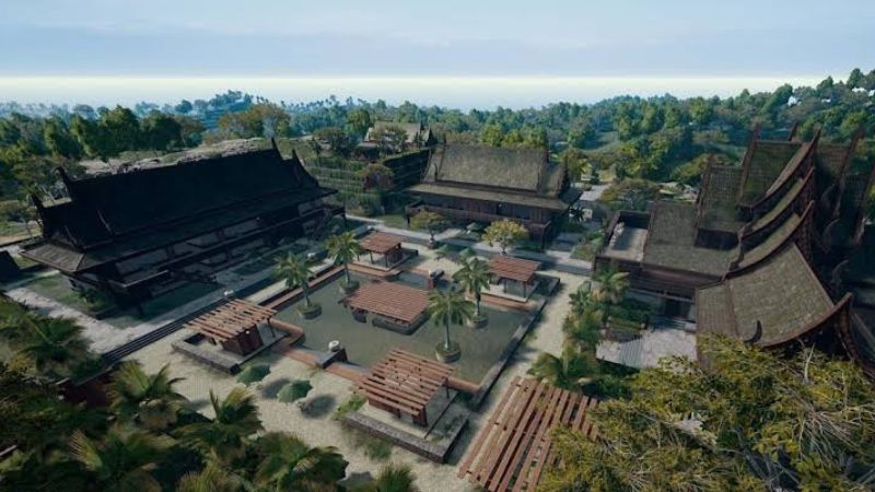 "An aerial view of Paradise Resort in Sanhok, PUBG Mobile's jungle map, showcasing traditional wooden structures, palm trees, and serene courtyards surrounded by lush greenery, reflecting the map's tropical environment."